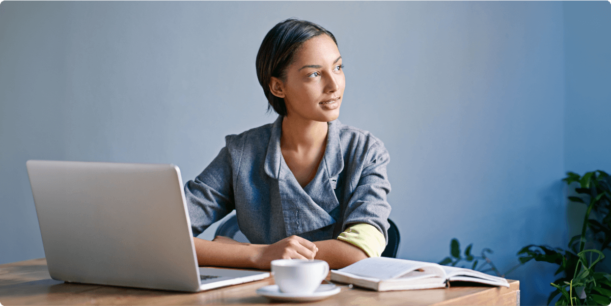 Eine Frau, die im Homeoffice arbeitet, mit einem Notizbuch, einem Laptop und einer Teetasse.