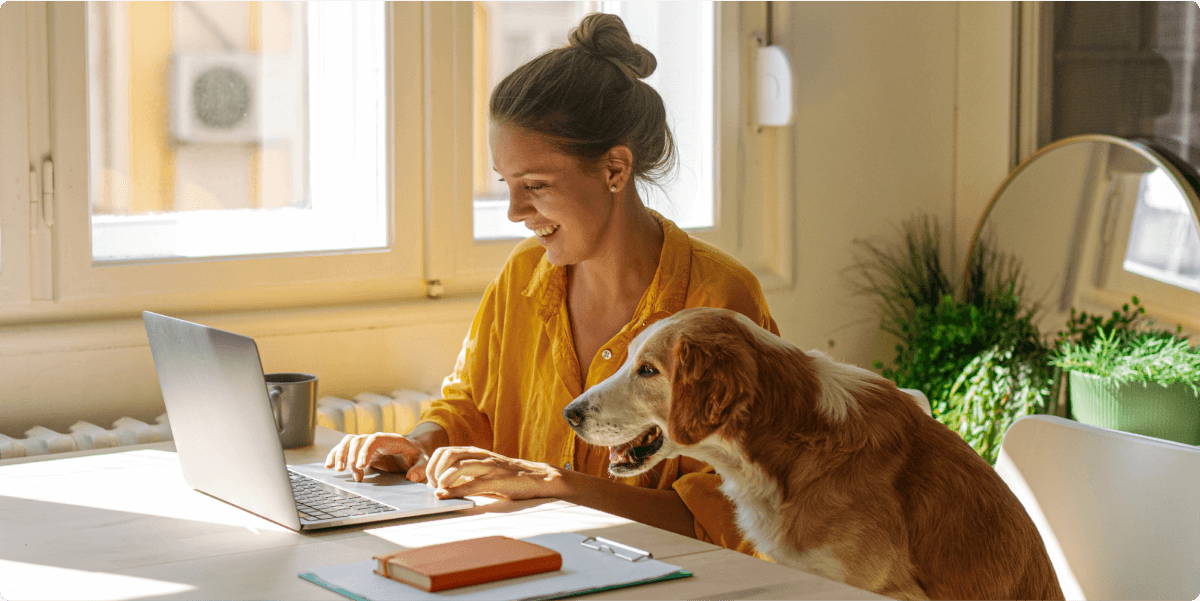 A woman working on her laptop with her dog nearby.