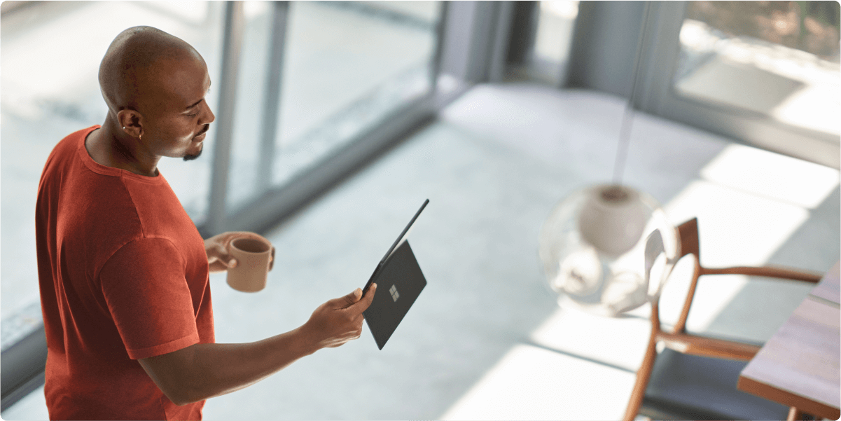 A man looking at a tablet while having his morning coffee. Sunlight streams in through the windows in his home.