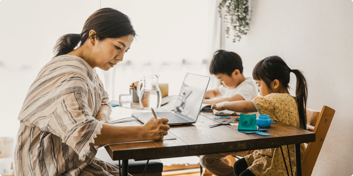 Una mujer que trabaja en la mesa del comedor con sus hijos, que están haciendo manualidades.