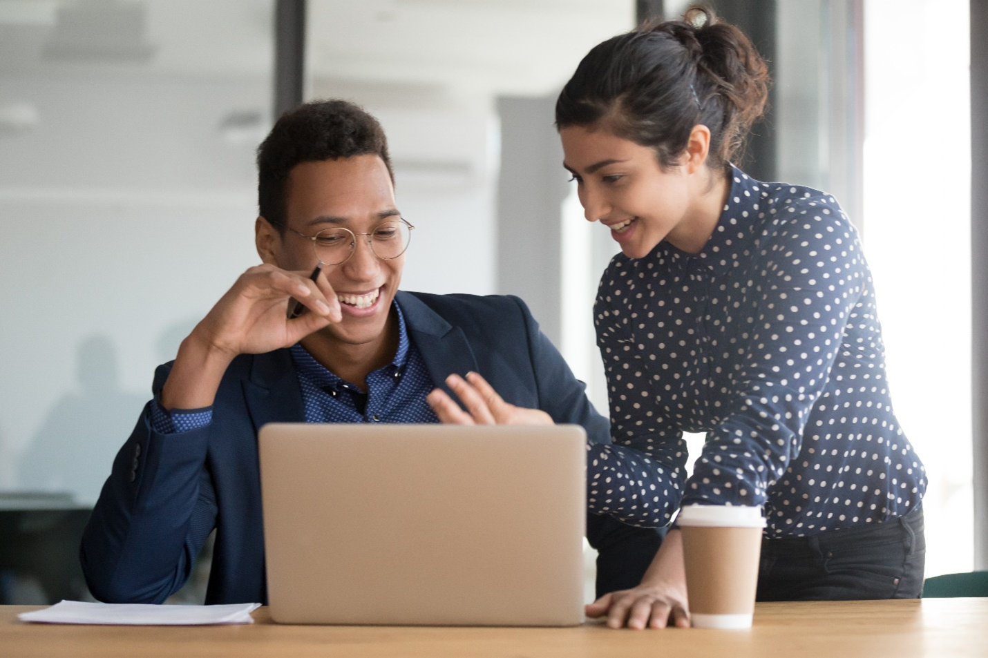 Une photo d’un homme et d’une femme souriant au bureau, regardant un ordinateur portable.