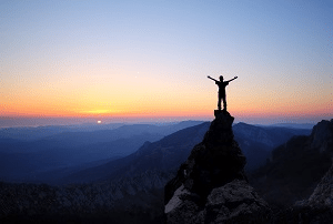 No exterior, o pôr do sol nas montanhas, com a silhueta de uma pessoa